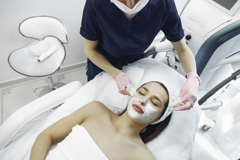 a woman getting a facial mask at a beauty salon, by Julian Allen, overlay, nurse, femalev beauty, mid view