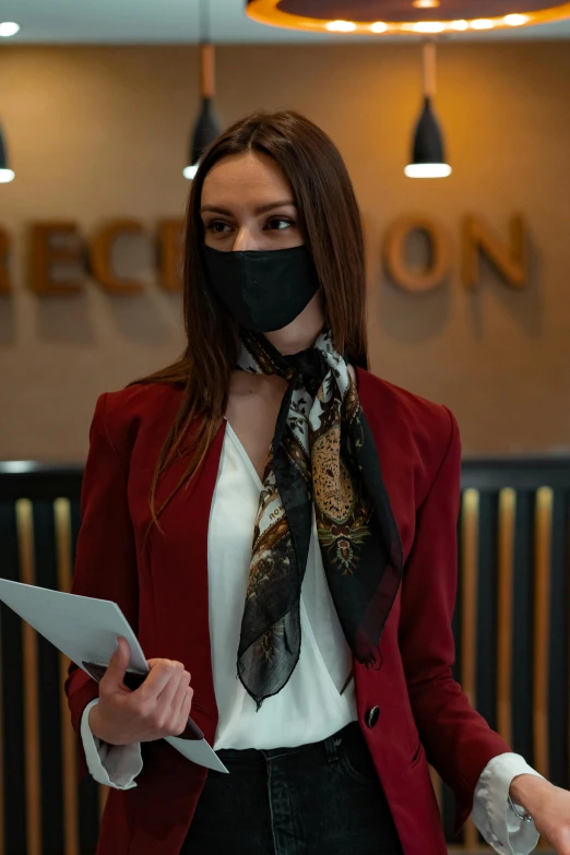 a woman wearing a face mask and holding a tablet, in a hotel hallway, creterion collection, black scarf, executive industry banner