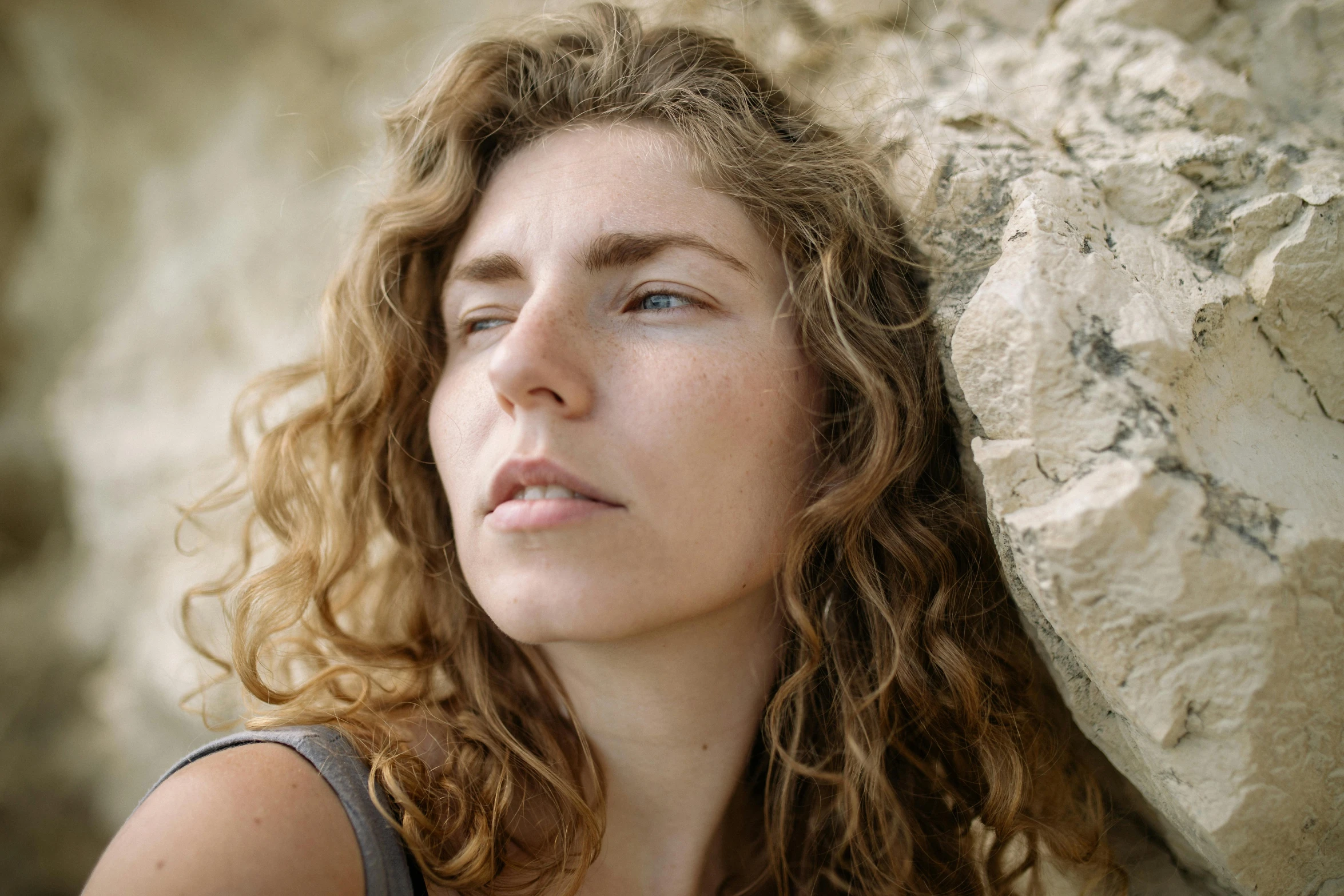 a woman with curly hair leaning against a rock, trending on pexels, exhausted face close up, looking upwards, isolde, portrait image