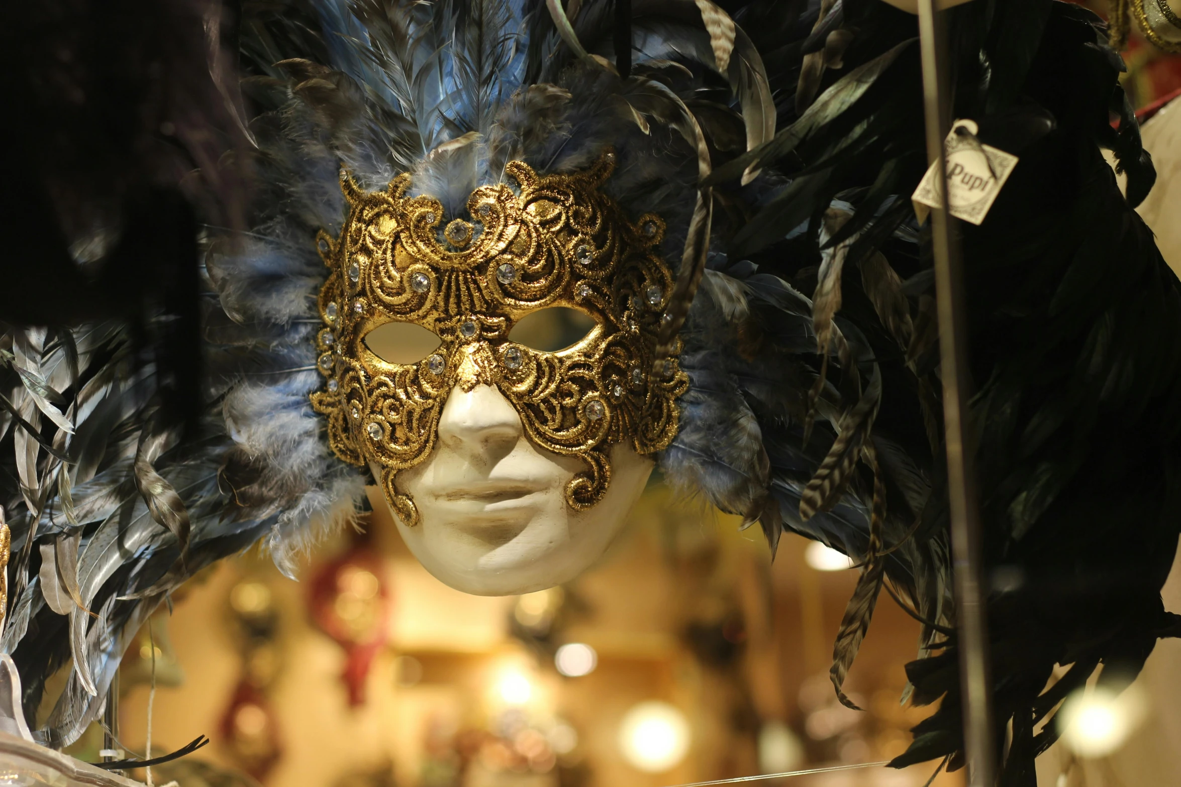 a close up of a mask with feathers on it, an album cover, inspired by Quirizio di Giovanni da Murano, pexels contest winner, baroque, shopwindows, over-shoulder shot, shades of gold display naturally, thumbnail