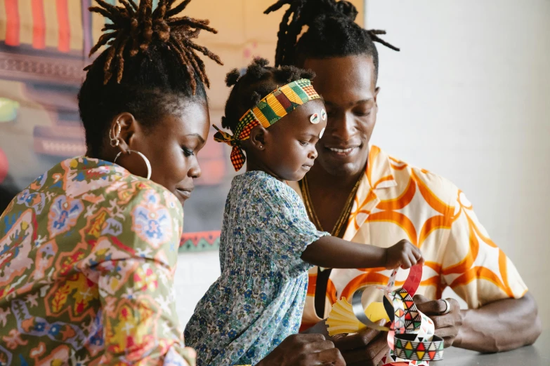 a couple of people that are sitting at a table, pexels contest winner, black arts movement, with a kid, rasta, toys, wearing an african dress