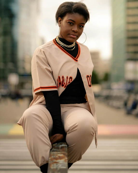 a woman sitting on top of a metal pole, an album cover, trending on unsplash, female baseball player, brown pants, full uniform, brown skin