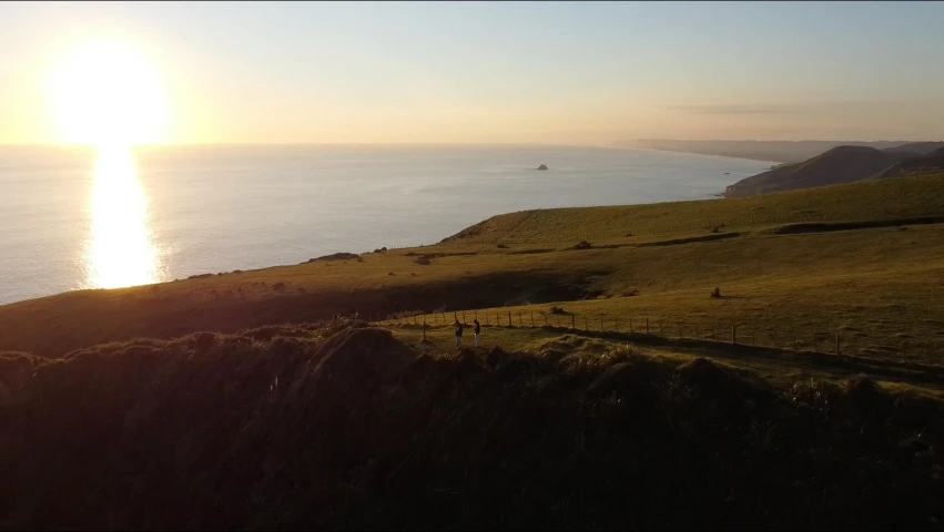 a large body of water sitting on top of a lush green hillside, a picture, pexels contest winner, happening, sun set, cliffs of dover, hd footage, people walking into the horizon