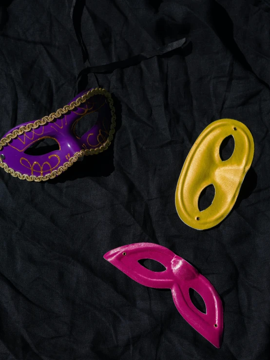 a couple of masks sitting on top of a black sheet, a colorized photo, trending on unsplash, yellow purple, detailed product image, hot pink and gold color scheme, toy photo