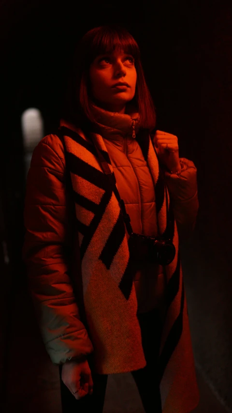 a woman that is standing in the dark, orange reflective puffy coat, red scarf, movie still 8 k, **cinematic