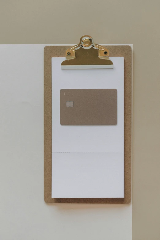 a clipboard with a piece of paper attached to it, by David Simpson, light - brown wall, at checkout, focus on card, rear facing