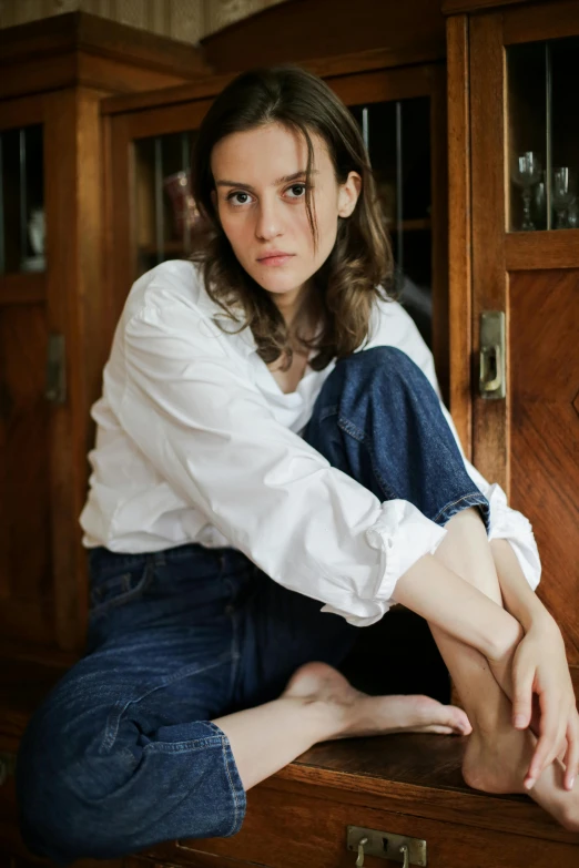 a woman sitting on top of a wooden suitcase, by Nina Hamnett, trending on unsplash, renaissance, white shirt and jeans, winona ryder, leaning on door, frown fashion model