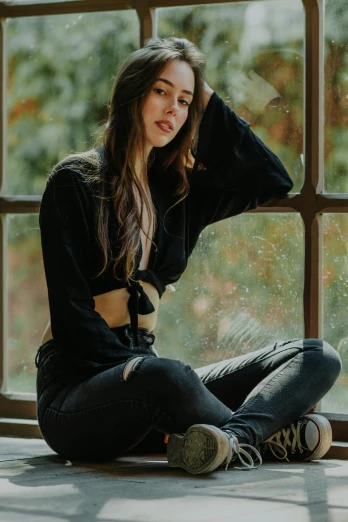 a woman sitting on the floor in front of a window, a picture, inspired by Elsa Bleda, trending on pexels, renaissance, wearing jeans and a black hoodie, young woman with long dark hair, wearing a cropped top, view(full body + zoomed out)