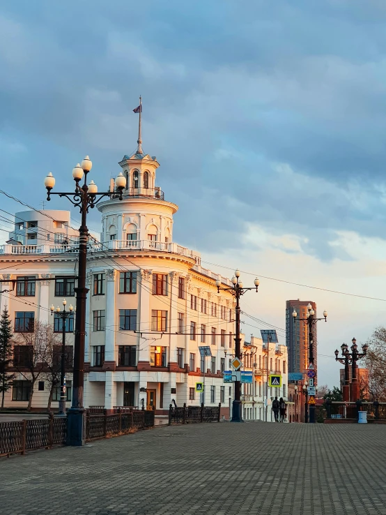 a clock tower sitting on the side of a road, inspired by Illarion Pryanishnikov, beautifully lit buildings, viewed from the harbor, square, taken in the early 2020s