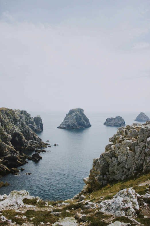 a man standing on top of a cliff next to a body of water, by Raphaël Collin, unsplash, les nabis, two medium sized islands, northern france, rocky foreground, asymmetrical spires
