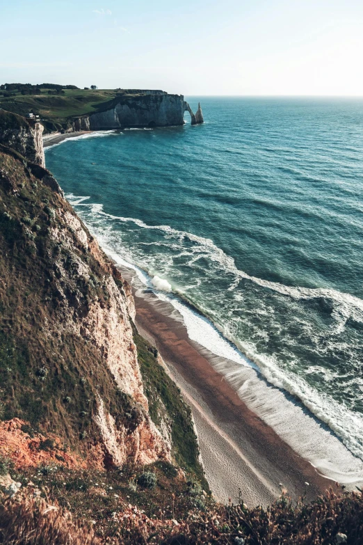 a man standing on top of a cliff next to the ocean, by Raphaël Collin, pexels contest winner, renaissance, normandy, slide show, drone footage, chalk cliffs above