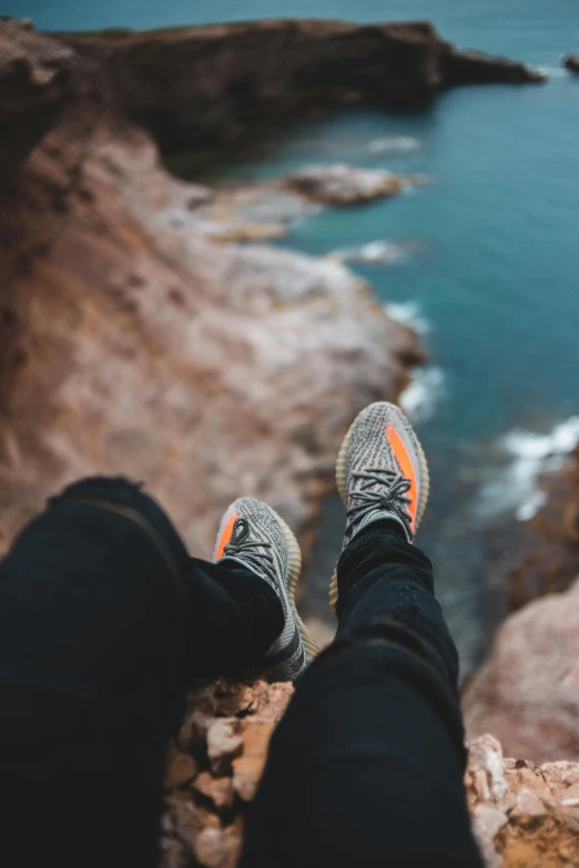 a person sitting on a rock overlooking the ocean, trending on pexels, sneaker photo, grey orange, head straight down, yeezy