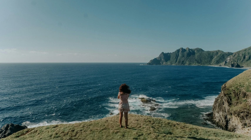 a woman standing on a cliff overlooking the ocean, pexels contest winner, happening, samoan features, low quality photo, various posed, on a bright day