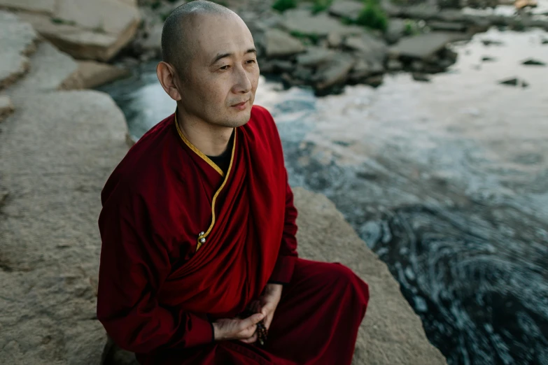 a man sitting on top of a rock next to a river, a portrait, unsplash, shin hanga, wearing red robes, avatar image, ukrainian monk, maggie cheung