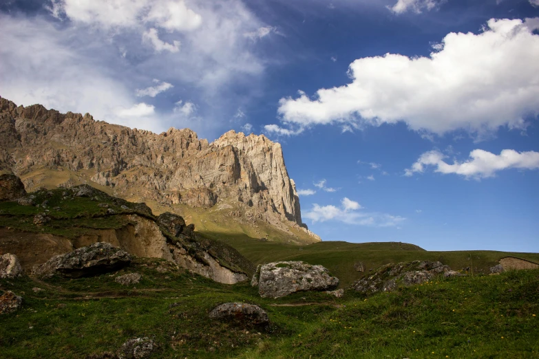 a grassy field with rocks and a mountain in the background, by Muggur, pexels contest winner, les nabis, caucasian, show from below, slide show, panorama