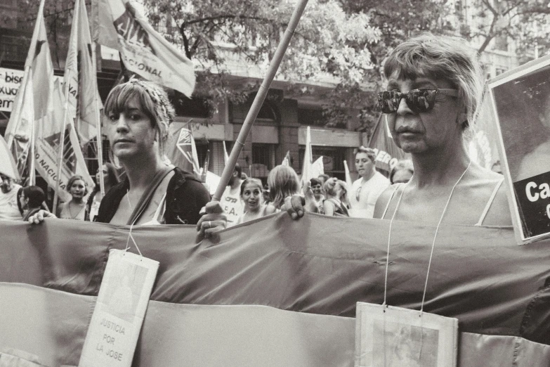 a black and white photo of a group of people holding a banner, by Luis Molinari, woman holding another woman, sad look, parade, manila