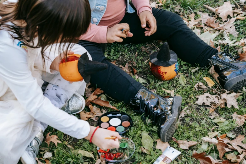 a couple of people that are sitting in the grass, a child's drawing, pexels contest winner, trick or treat, painted nails, spray paint, autumn leaves on the ground