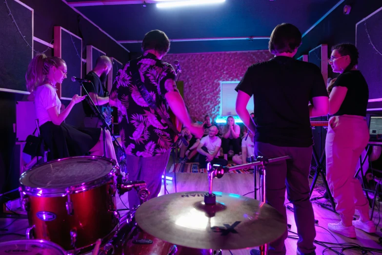 a group of people standing around a drum set, brightly lit purple room, profile image, teenager hangout spot, lachlan bailey