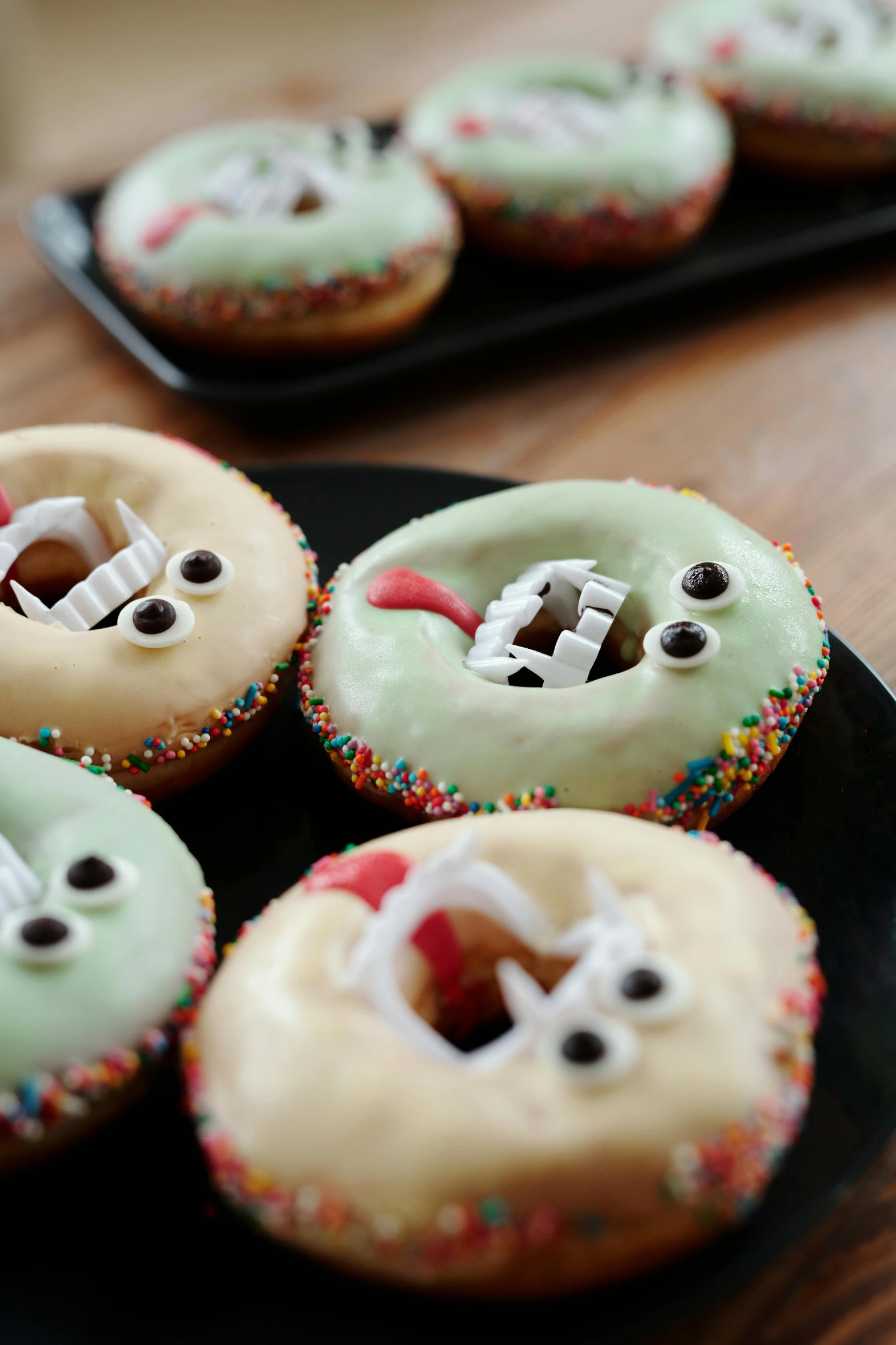 a black plate topped with donuts covered in frosting, inspired by Johann Rudolf Byss, reddit, zombie ghouls, so cute, middle close up shot, halos