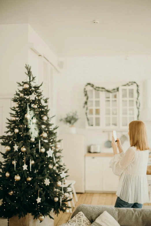 a woman standing in a living room next to a christmas tree, pexels contest winner, light and space, white, food, profile image, kids