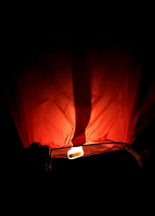 a person holding a cell phone in the dark, hanging from a hot air balloon, the color red, dim lantern, rectangle
