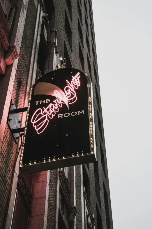 a neon sign hanging from the side of a building, sitting across the room, signature on the bottom, soggy, sparkly