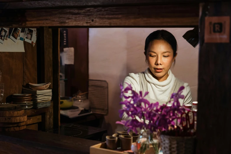 a woman standing behind a counter with a vase of flowers, pexels contest winner, shin hanga, tea drinking and paper lanterns, lucy liu portrait, close to night, profile image