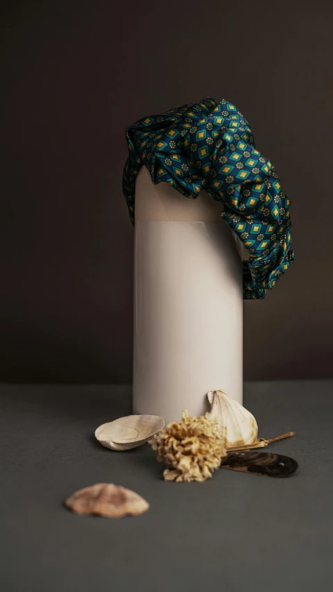 a white vase sitting on top of a table, an album cover, inspired by Sarah Lucas, unsplash, hyperrealism, patterned clothing, food styling, cloth head wrap, teal cloth