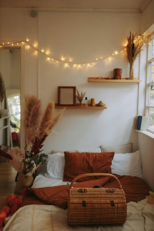 a bed with a basket on top of it next to a window, inspired by Elsa Bleda, unsplash contest winner, light and space, floating lights, orange and white color scheme, cottagecore hippie, apartment of an art student