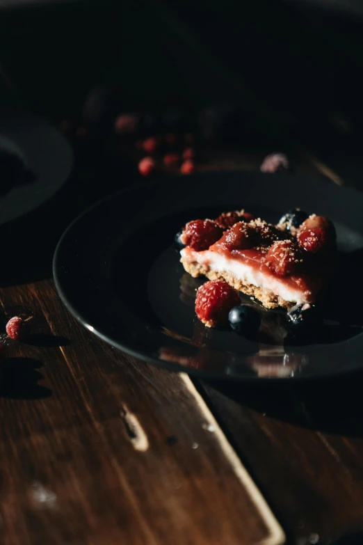 a piece of cake sitting on top of a black plate, pexels, berries inside structure, on wooden table, lifestyle, ue 5