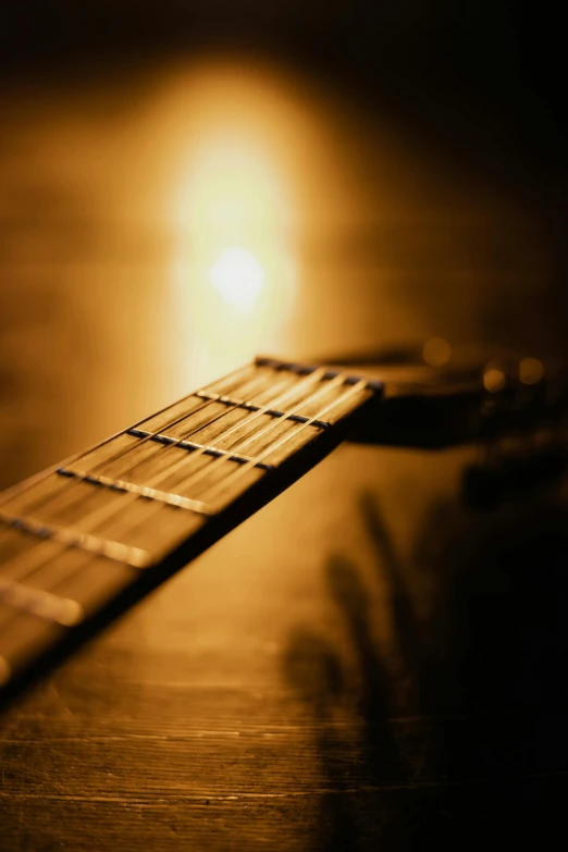 a guitar sitting on top of a wooden table, golden dappled dynamic lighting, paul barson, stockphoto, soft light - n 9