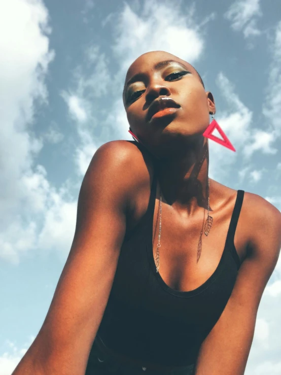 a beautiful young woman sitting on top of a skateboard, by Dulah Marie Evans, trending on pexels, afrofuturism, ankh pendant, face looking skyward, shaved hair, wearing a cropped black tank top