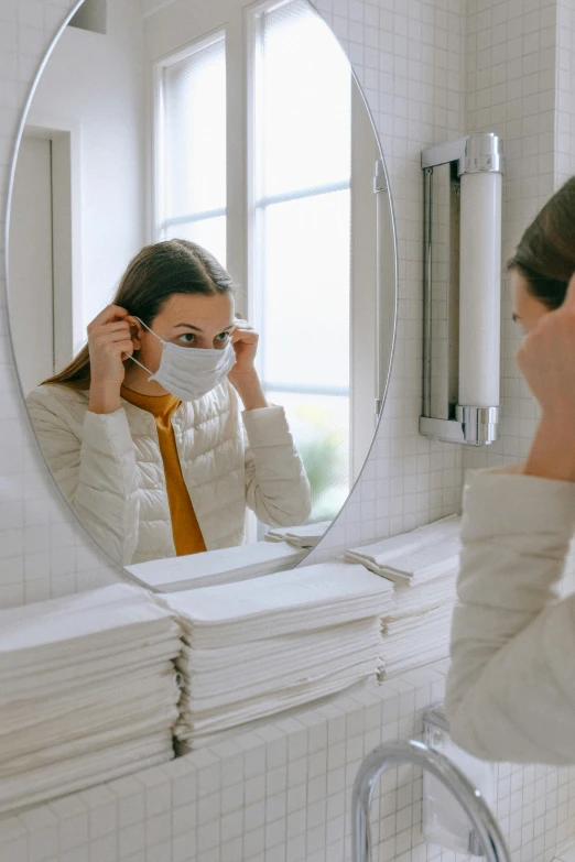 a woman putting on a mask in front of a mirror, multiple layers, clean and simple, staring, grey