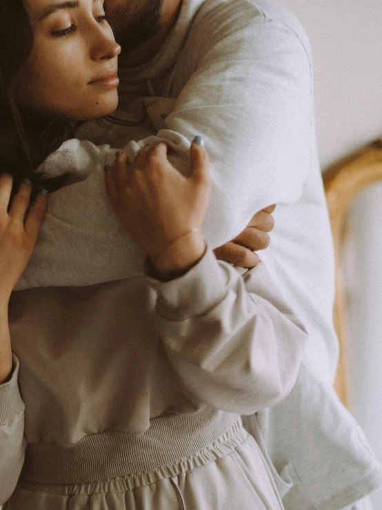 a man and a woman hugging each other, trending on unsplash, beige hoodie, wearing white silk, woman holding another woman, low quality photo