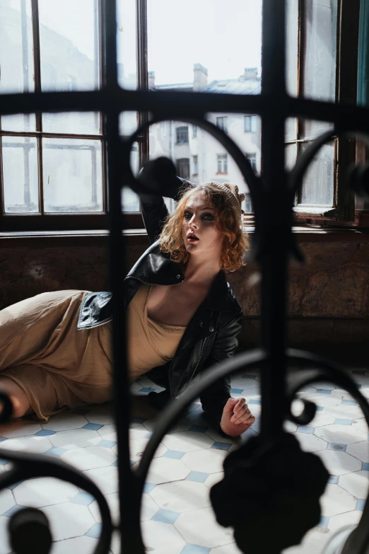 a woman laying on the floor in front of a window, an album cover, pexels contest winner, standing astride a gate, pale skin curly blond hair, wearing a leather trench coat, photography alexey gurylev