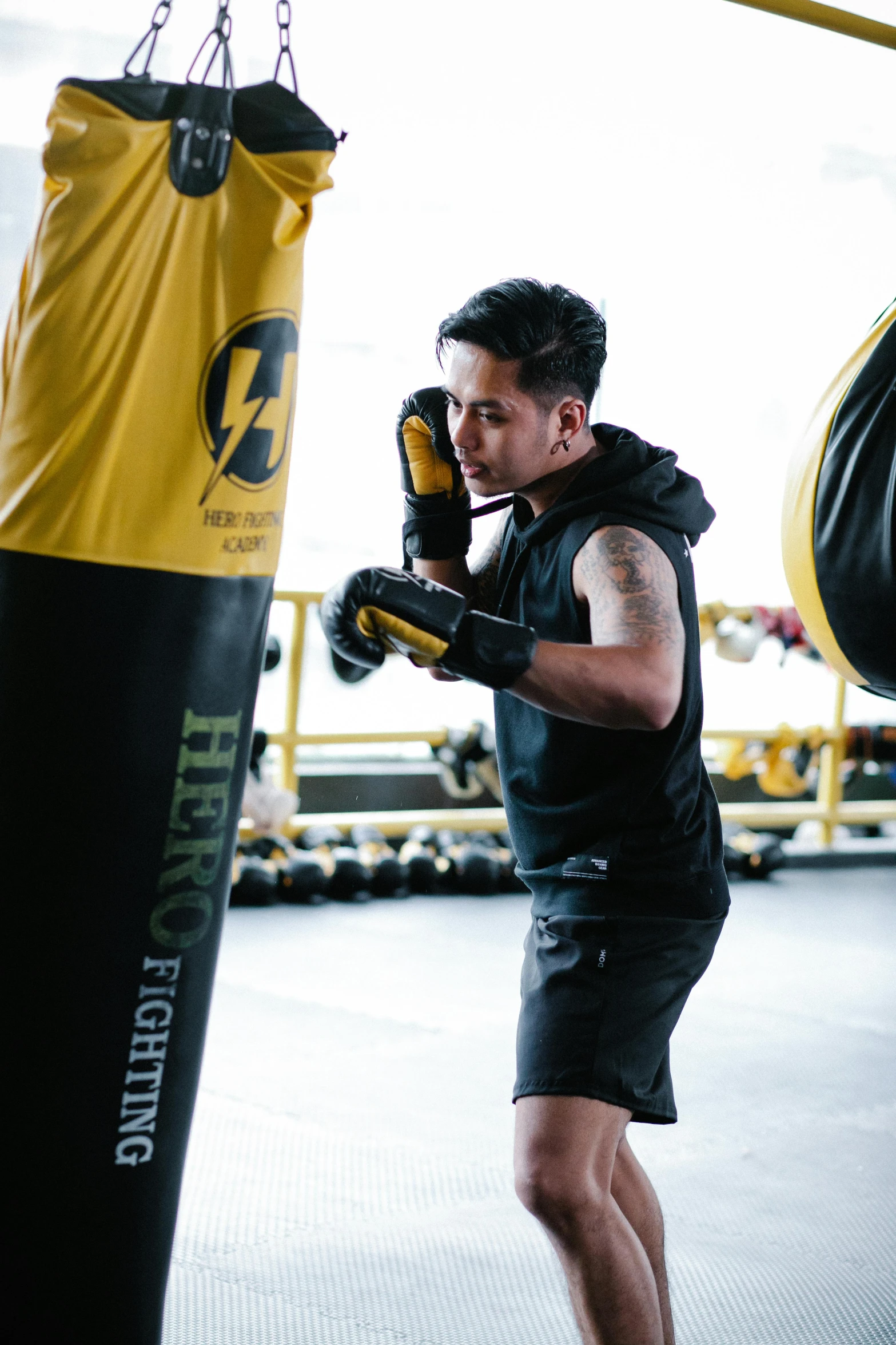 a man standing next to a punching bag, by Robbie Trevino, happening, black and yellow tracksuit, hero, manuka, action with run and fight