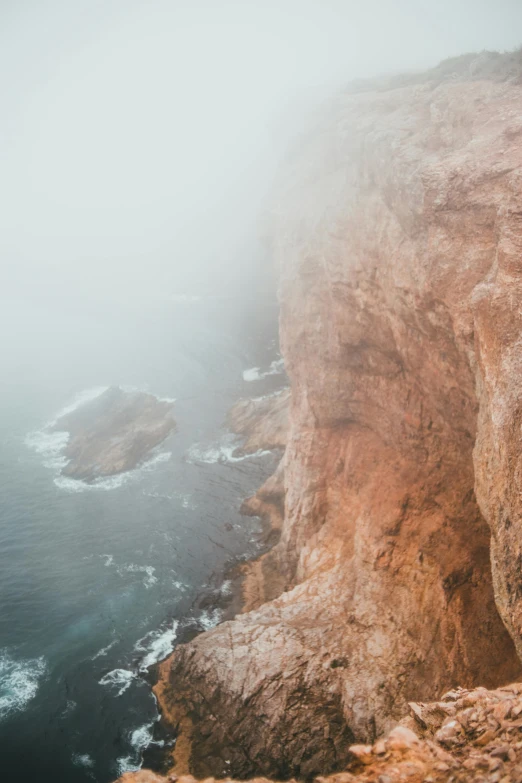 a man standing on top of a cliff next to the ocean, by Matt Cavotta, trending on unsplash, romanticism, uneven dense fog, beige mist, close up shot from the top, multiple stories