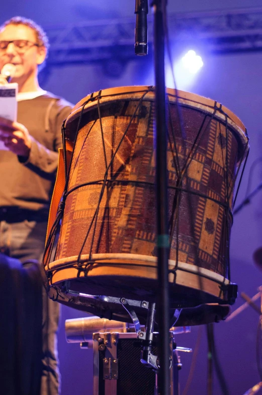 a man standing next to a drum on a stage, by Jan Tengnagel, happening, in thick layers of rhythms, local close up, concert, holding a tower shield