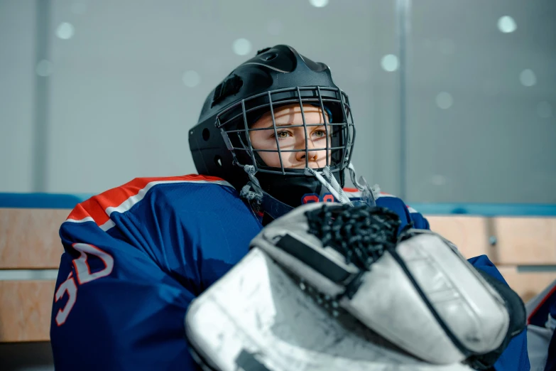 a person sitting on a bench with a hockey helmet on, a picture, shutterstock, full ice hockey goalie gear, teenage girl, holding it out to the camera, performance