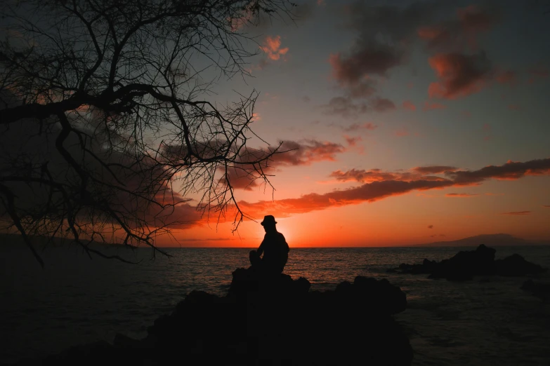 a man sitting on top of a rock next to the ocean, pexels contest winner, romanticism, silhouette :7, maui, orange and red sky, multiple stories