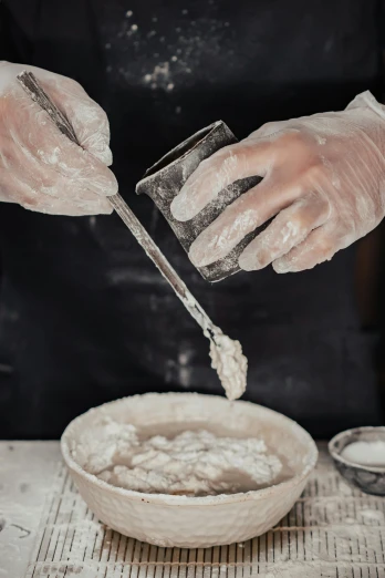 a person is sprinkling flour into a bowl, a marble sculpture, inspired by Jean-Baptiste Pater, process art, gloves on hands, intense look, beakers, traditional medium
