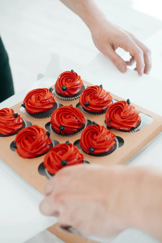 a close up of a tray of cupcakes on a table, inspired by Tex Avery, pexels, art nouveau, black and red dress, spiraling, sleek hands, baking artwork