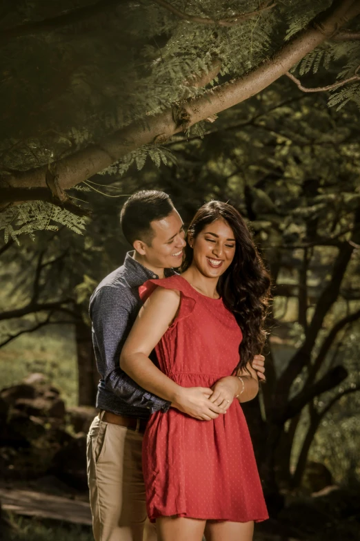 a man standing next to a woman in a red dress, a picture, pexels contest winner, with a tree in the background, sydney park, asian man, brown