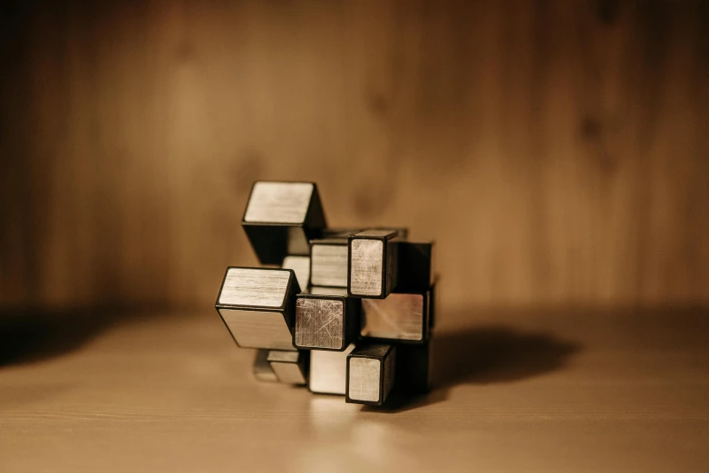 a pile of metal cubes sitting on top of a wooden table, an abstract sculpture, inspired by Ernő Rubik, unsplash, mirrored, high quality photo, an instrument, soft light from the side