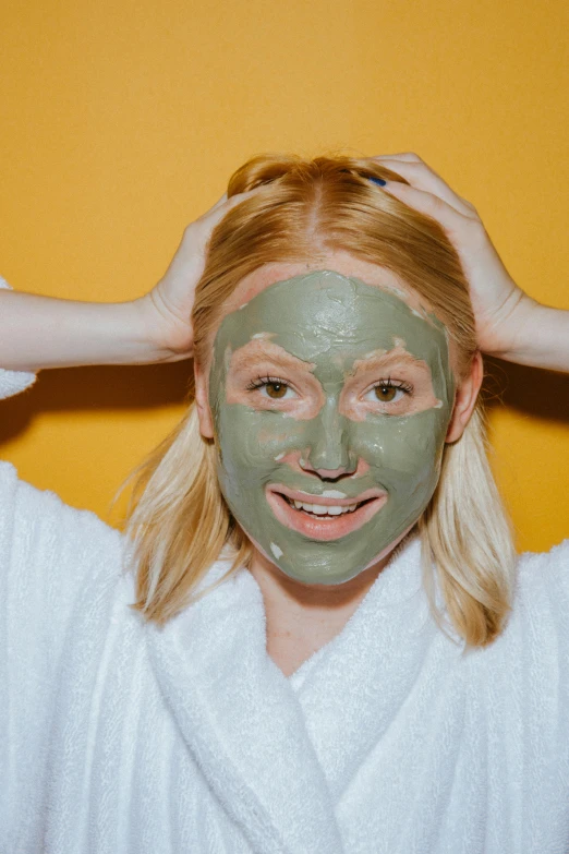 a woman putting a facial mask on her face, a colorized photo, by Julia Pishtar, trending on pexels, sage green, happily smiling at the camera, covered in, goop