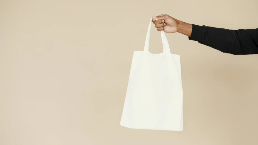 a man holding a white bag in his hand, by Carey Morris, minimalism, presenting wares, riyahd cassiem, without text, cream paper