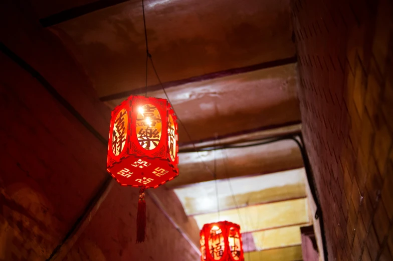 a couple of red lanterns hanging from a ceiling, by Julia Pishtar, alleys, warm glow, hua cheng, indoor picture