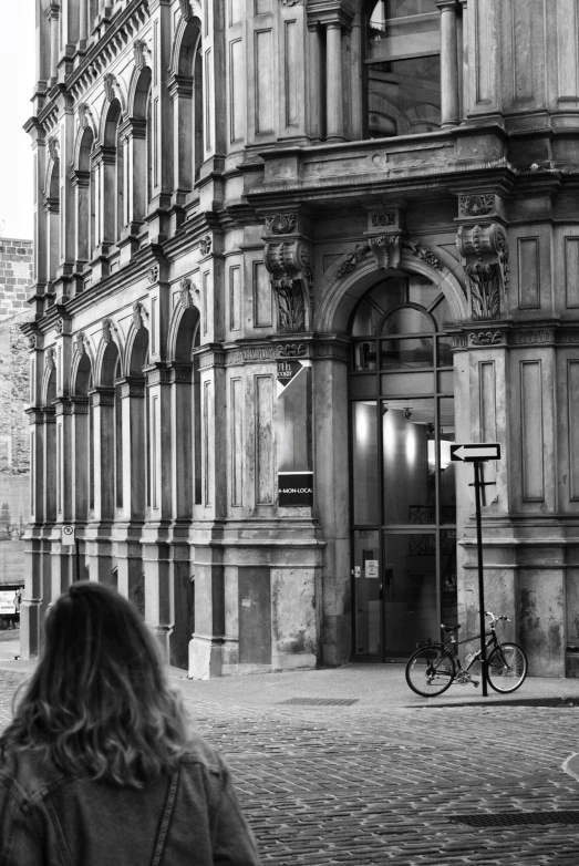 a woman walking down a street past a tall building, a black and white photo, pexels contest winner, realism, lviv, bicycle, old library, manchester