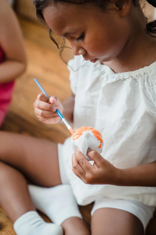 a little girl sitting on the floor holding a toothbrush, inspired by Andrea del Sarto, pexels contest winner, process art, holding a tangerine, tissue ornament, paints, carefully crafted