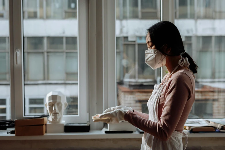 a woman wearing a face mask standing in front of a window, pexels contest winner, porcelain sculpture, inspect in inventory image, chemistry, profile image